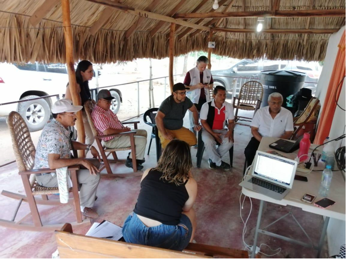 A group of people sit outside on a covered patio gathered around two laptop computers.