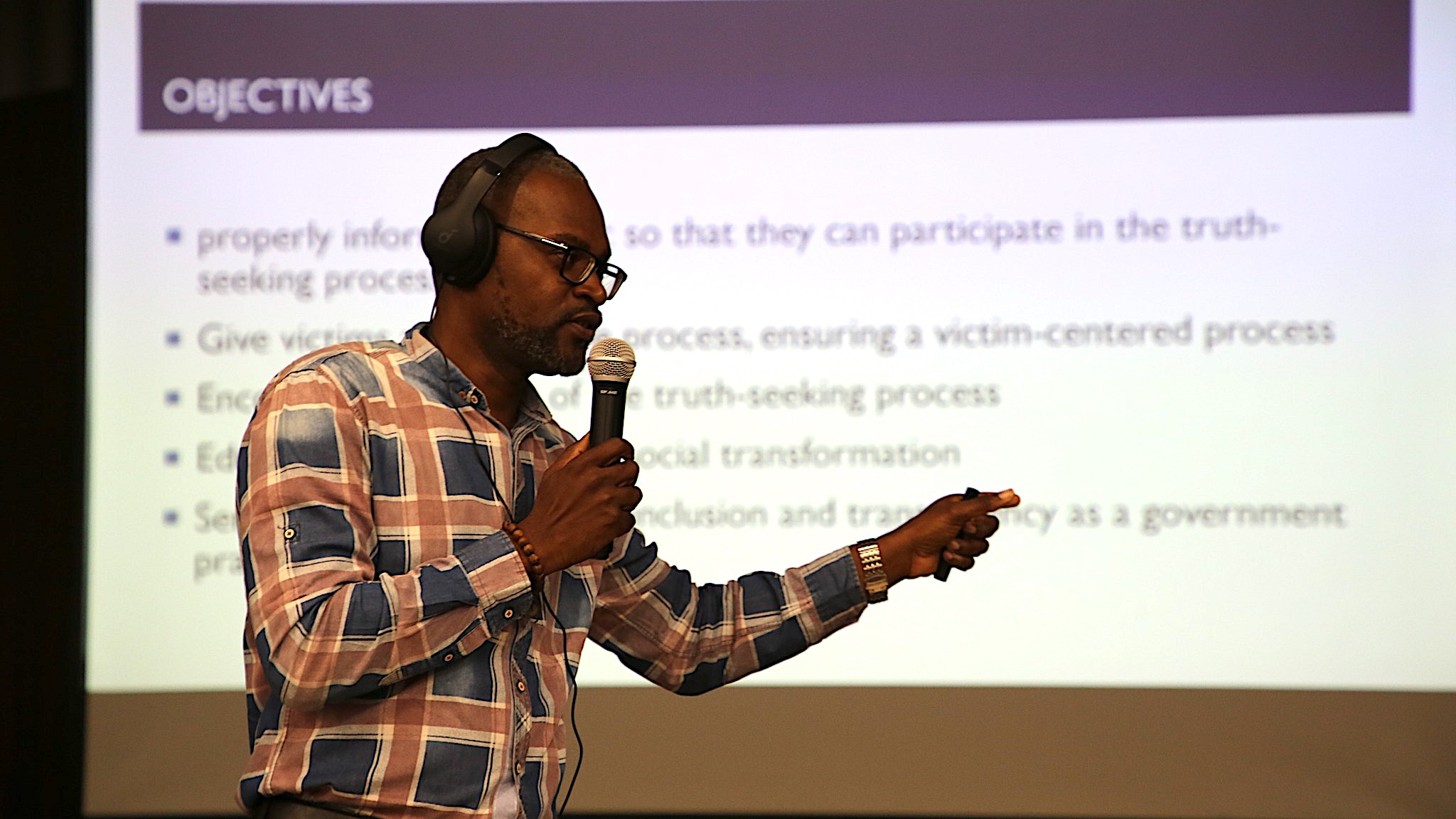 Un homme se tient devant un écran avec une présentation tenant un microphone.