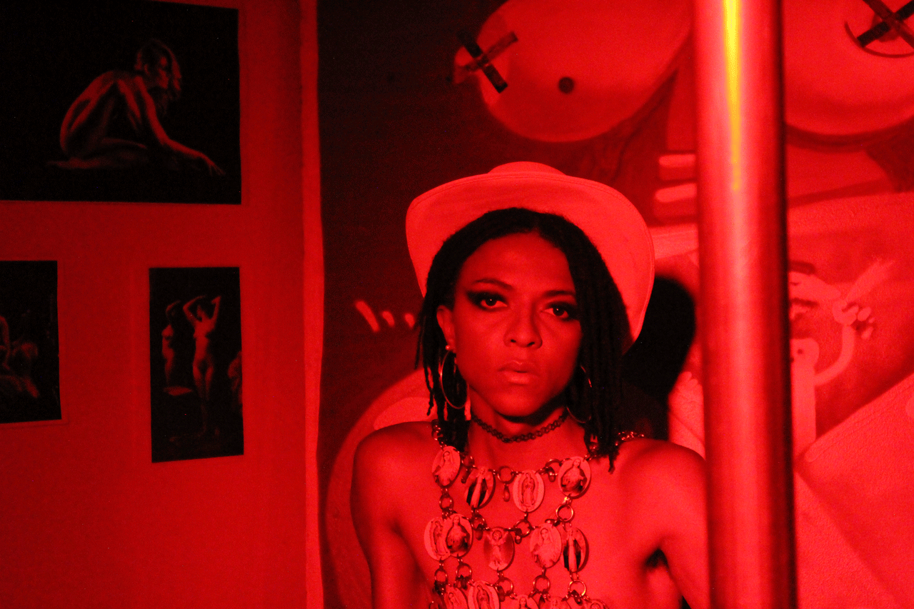 A Black woman sits in the right of the frame under a red light