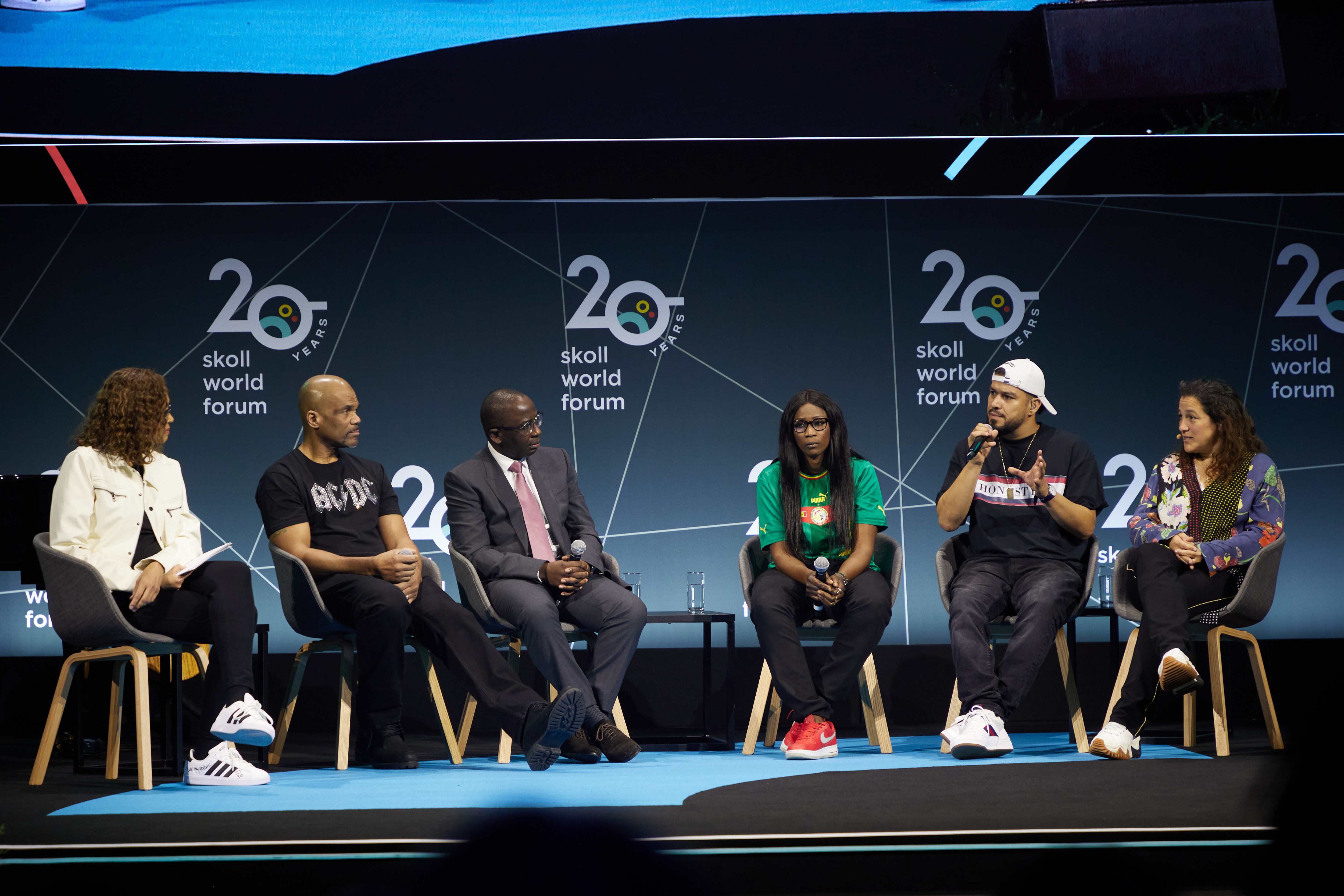 Six people are seated in row of chairs on a stage engaged in a panel discussion.