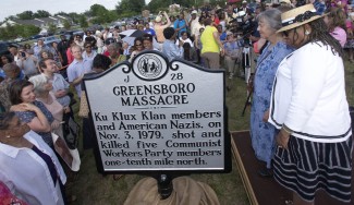 People gather around a plaque marking the Greenboro Massacre outside during an inaugural ceremony